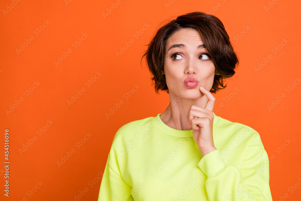 Photo of cheerful young happy woman look empty space minded lips pouted isolated on orange color background Photo of cheerful young happy woman look empty space minded lips pouted isolated on orange color background