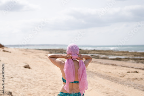 Woman on beach tying pink headscarf, cancer