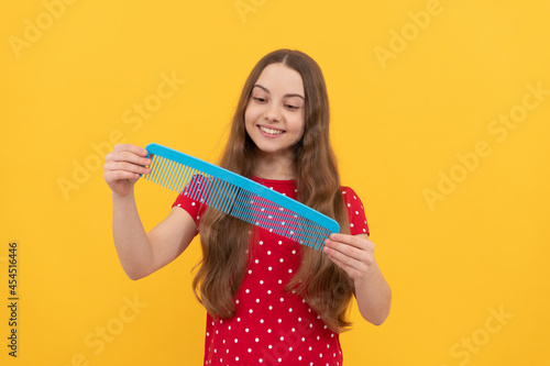happy kid brushing long hair with comb on yellow background  haircare