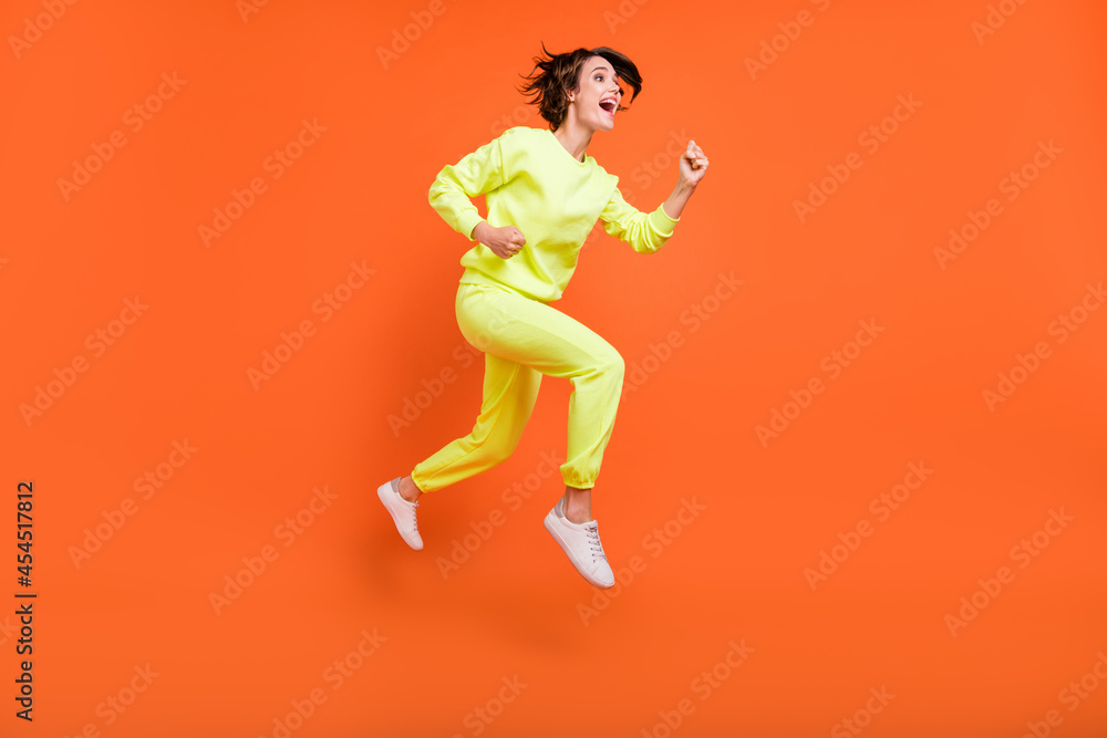 Full length body size view of attractive cheerful girl jumping running action isolated over bright orange color background