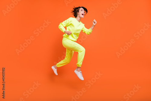 Full length body size view of attractive cheerful girl jumping running action isolated over bright orange color background © deagreez