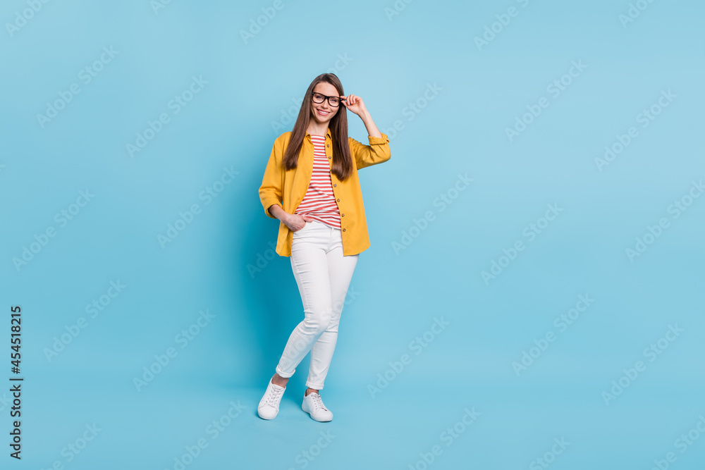 Full length photo of young attractive woman happy positive smile confident hand touch glasses isolated over blue color background Full length photo of young attractive woman happy positive smile confident hand touch glasses isolated over blue color background