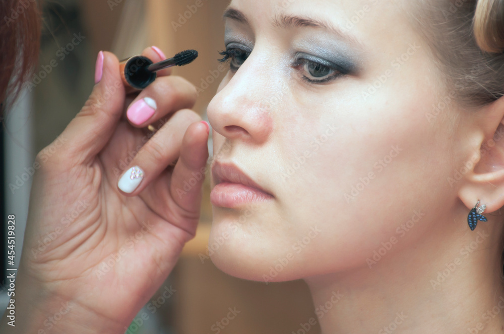 the makeup artist's hand applies makeup to the face of a young woman. The concept of facial care, make-up, advertising of makeup artist services.