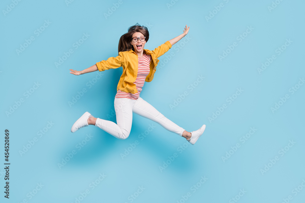 Full length profile side photo of young woman happy positive smile fly air hands wings jump isolated over blue color background