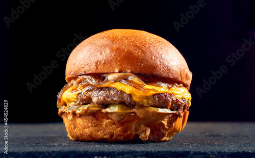 Juicy burger with beef, cheese, caramelized onions and tomato, sauce on a dark background.