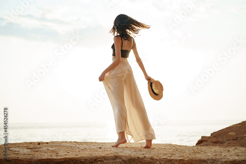 Young stylish woman standing on cliff at the sea at sunset