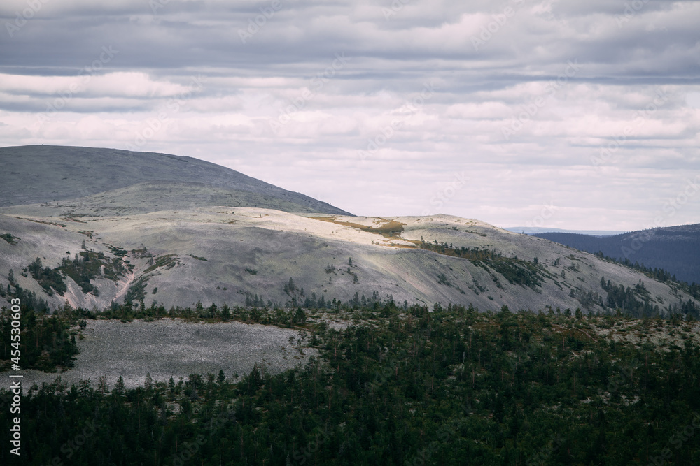 Peaceful landscape in the mountains of Lapland, with patches of sunlight on a fell and clouds in the sky.