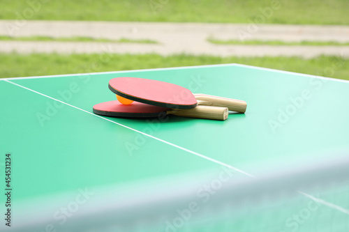 Tennis rackets and ball on ping pong table in park