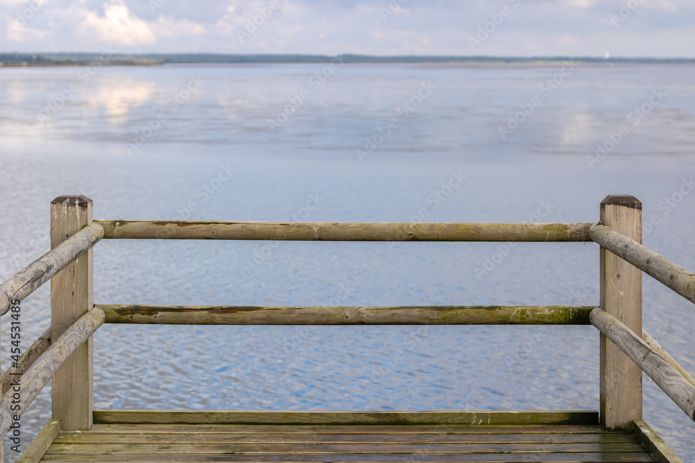 Obraz premium A wooden pier by a river, pond, lake with blue shiny water. Location for walks of city dwellers, relaxation outdoors. Rope fence near the lake