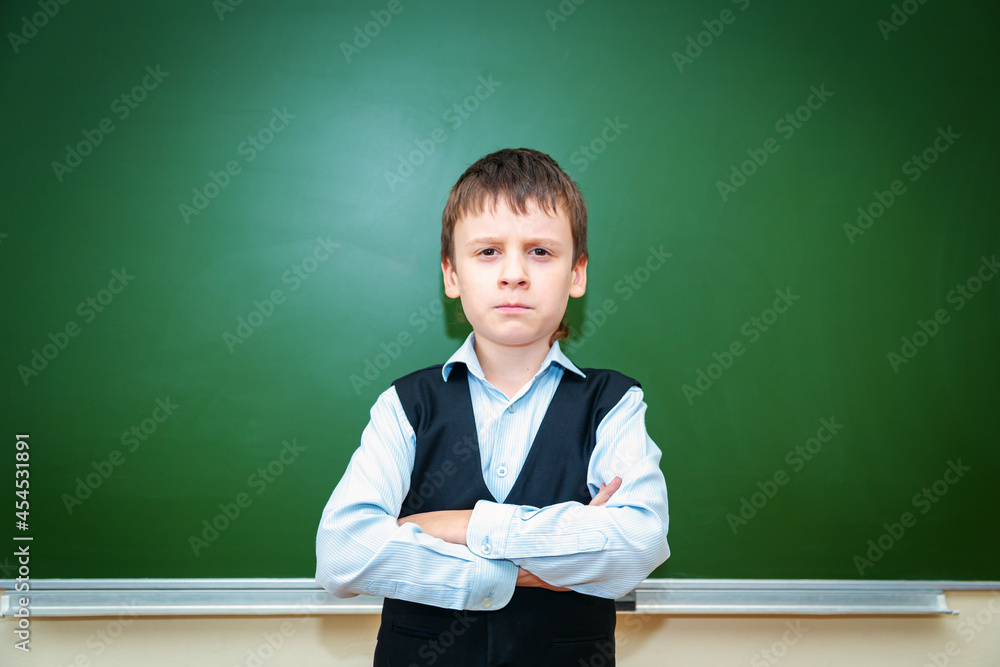 Serious schoolboy near the green school board in the classroom. Serious schoolboy near the green school board in the classroom.
