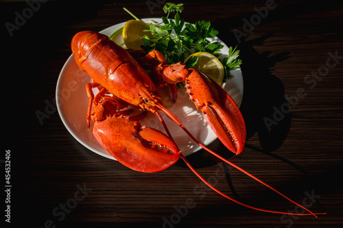 Steamed fresh red lobster on a white plate with parsley and lemon on a sunny day on a black table. Seafood. View from above. Copy space for your text.