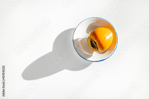 Ripe persimmon on white plate and long shadow on white table