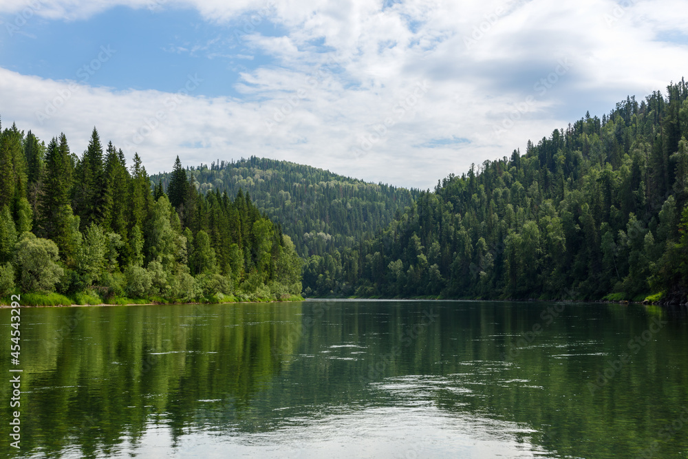 A river among a coniferous forest, mountains in the background. Daytime landscape