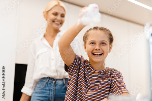 White mother and daughter smiling while washing dishes together