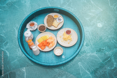 Floating breakfast in swimming pool. Healthy breafast served on the table relaxing in calm pool water, by tropical resort pool, summer beach luxury lifestyle