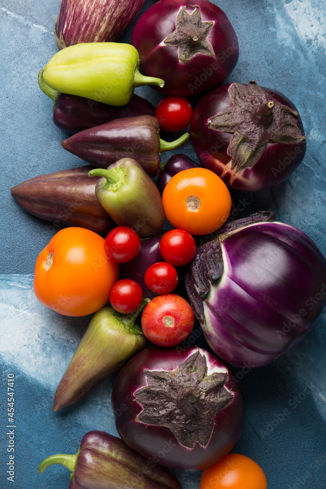 Radishes, tomatoes, cherry tomatoes, round eggplants, peppers, green tops on a blue background. Mix of different vegetables on a beautiful background.
