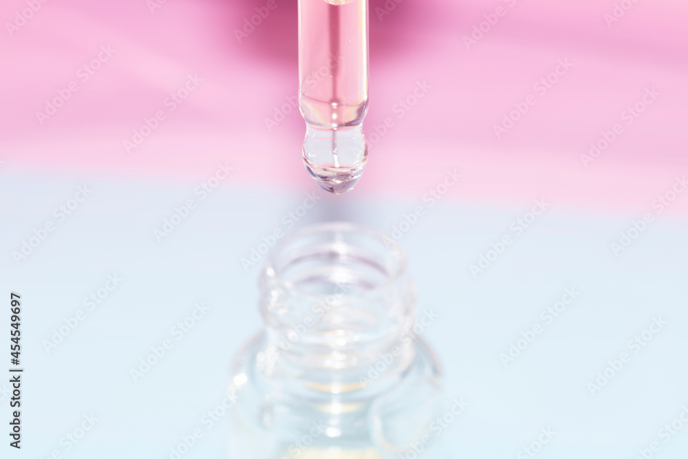 detail of face serum pouring out of pipette over a bottle on a pink and blue background detail of face serum pouring out of pipette over a bottle on a pink and blue background