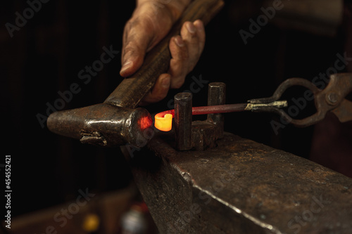 Close-up working powerful hands of male blacksmith forge an iron product in a blacksmith. Hammer, red hot metal and anvil. Concept of labor, retro professions