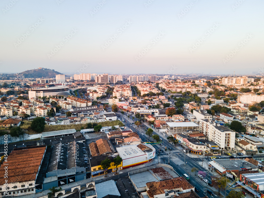 Imágem aérea da Avenida Dom Hélder Câmara com residências, industria e comércio com por do sol ao fundo na zona norte da cidade do Rio de Janeiro.
