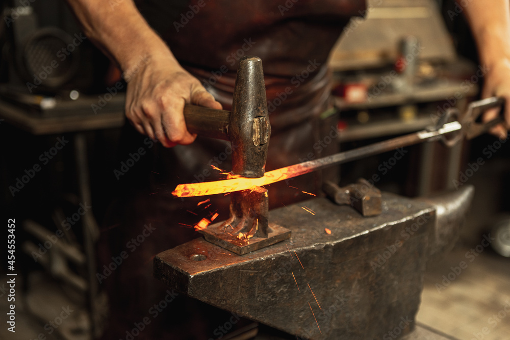 Close-up working powerful hands of male blacksmith forge an iron product in a blacksmith. Hammer, red hot metal and anvil. Concept of labor, retro professions Close-up working powerful hands of male blacksmith forge an iron product in a blacksmith. Hammer, red hot metal and anvil. Concept of labor, retro professions