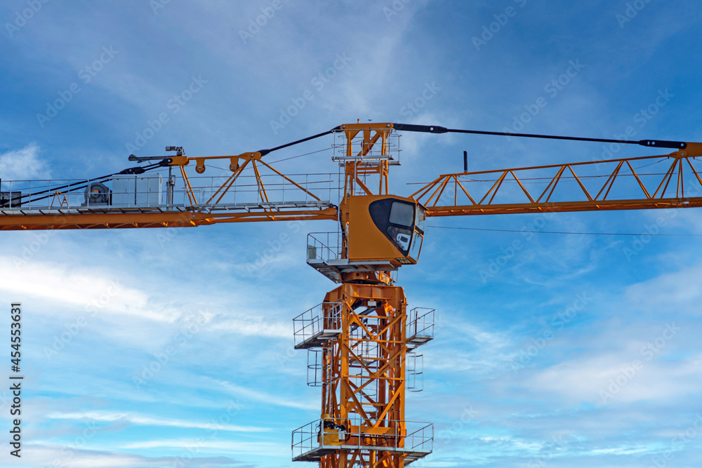 The top of the construction crane on the background of the blue sky with white clouds