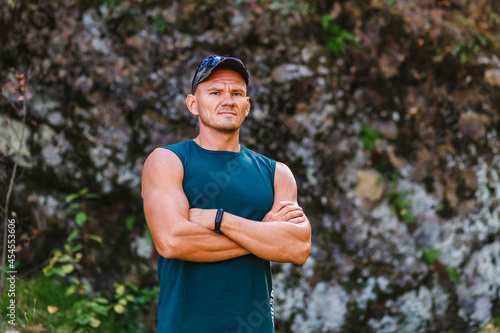 strong muscular man in a green sleeveless shirt stands against a cliff in the fall. freedom and nature