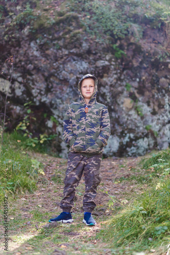 nine-year-old boy in a toast and a khaki hood stands tall on a hike in the mountains in the fall.