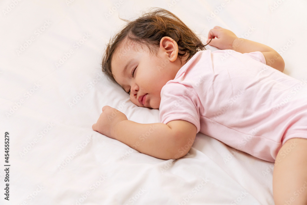 Little baby girl 12 months wearing pink cloth sleeping on white bed at home. Adorable one year old toddler mixed race asleep having good dream resting in the bedroom. Little baby girl 12 months wearing pink cloth sleeping on white bed at home. Adorable one year old toddler mixed race asleep having good dream resting in the bedroom.