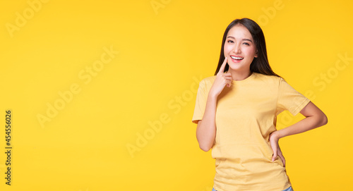Cheerful young woman use finger pointing to her head looking at product or empty copy space while standing over isolated on yellow background © kaew6566