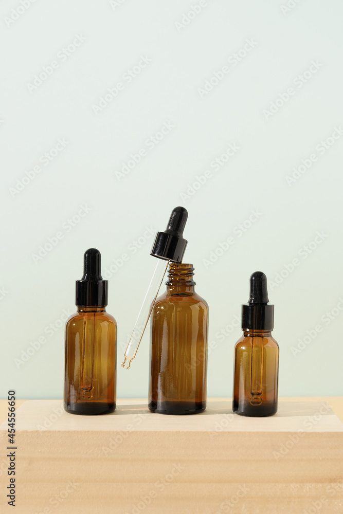 Transparent three glass bottles essential oil with dropper on stone on wooden and blue background. Vertical format. Close up. Transparent three glass bottles essential oil with dropper on stone on wooden and blue background. Vertical format. Close up.