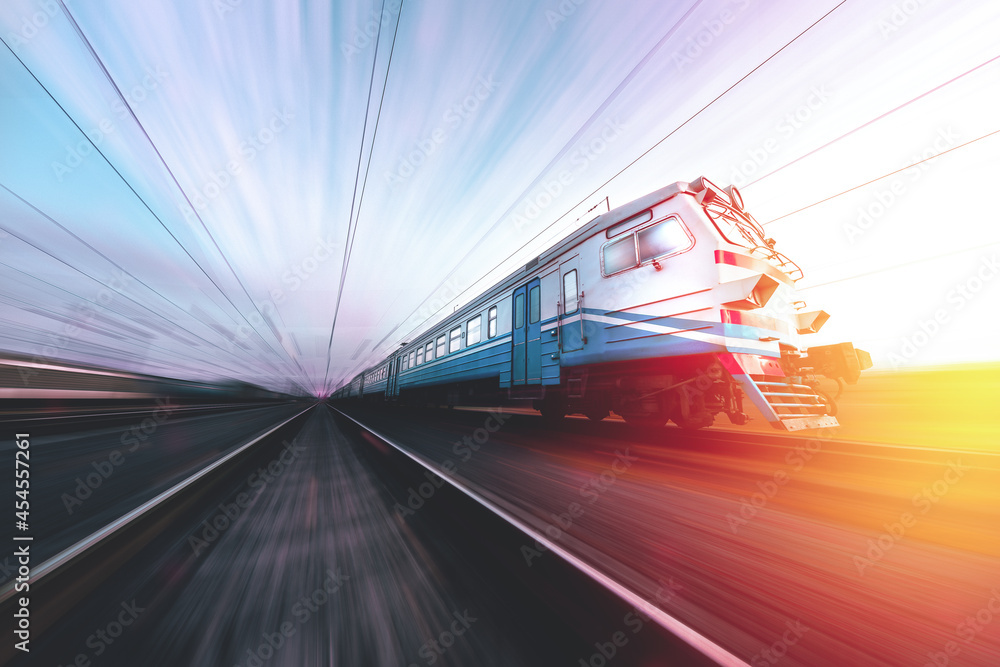 Fototapeta premium Old suburban train in motion against the background of sunrise - sunset. Ukrainian railway. Passenger train at speed