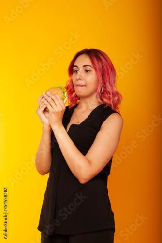 a girl with pink hair of European appearance looks at the burger biting her tongue licking wants to eat it