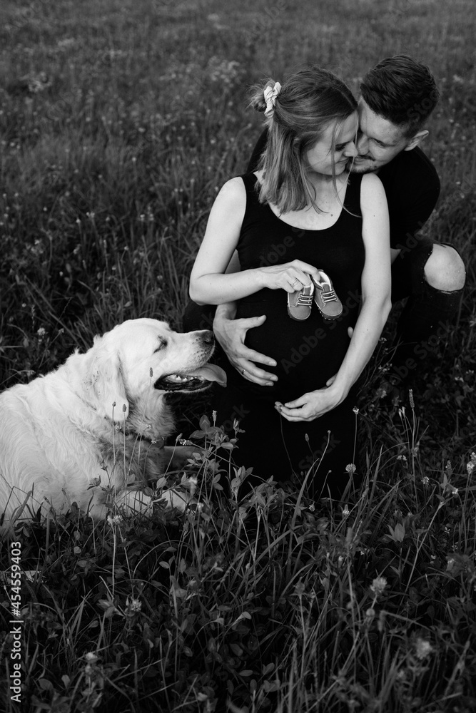 Young man hugs his pregnant wife, who is holding baby shoes in her ...