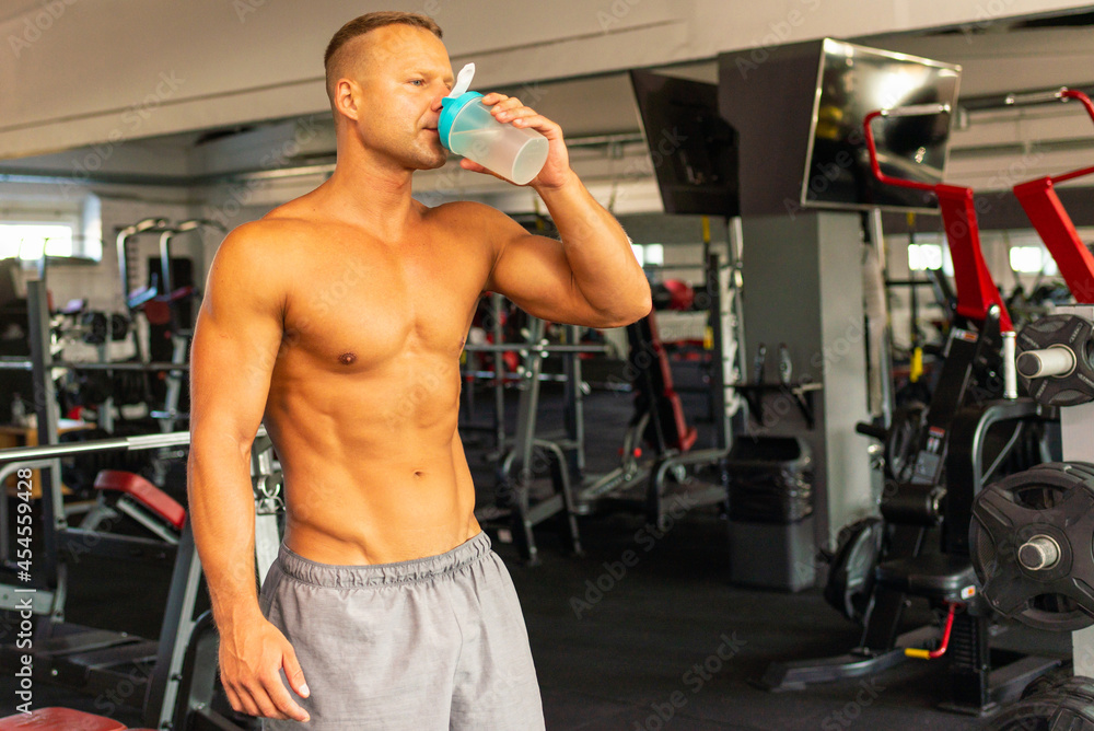 Young caucasian man drinking water after exercise.man in the gym drinking from the shaker. Young caucasian man drinking water after exercise.man in the gym drinking from the shaker.