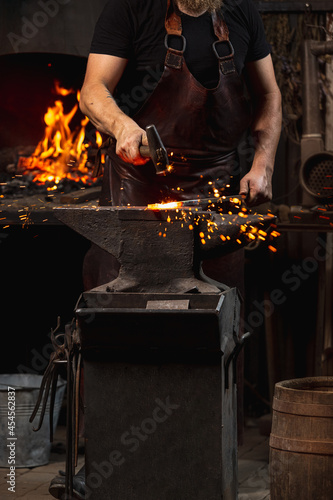 Cropped shot of man, blacksmith working on creating handmade metal product at family smithy. Concept of labor, retro professions, power, beauty photo