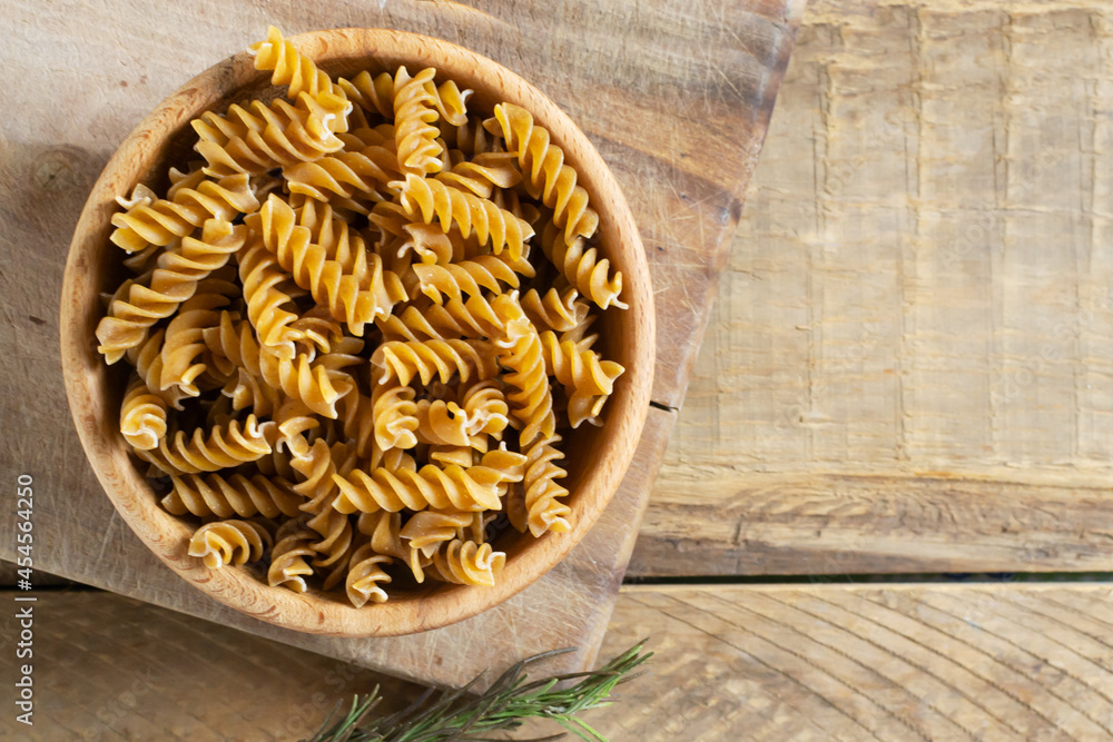 Raw fusilli in a wooden bowl on a cutting board on a wooden table. Rustic style. Horizontal orientation. Italian food concept. Top view. Copy space.