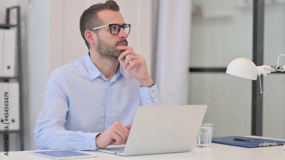 Middle Aged Man Thinking While using Laptop at Work Middle Aged Man Thinking While using Laptop at Work