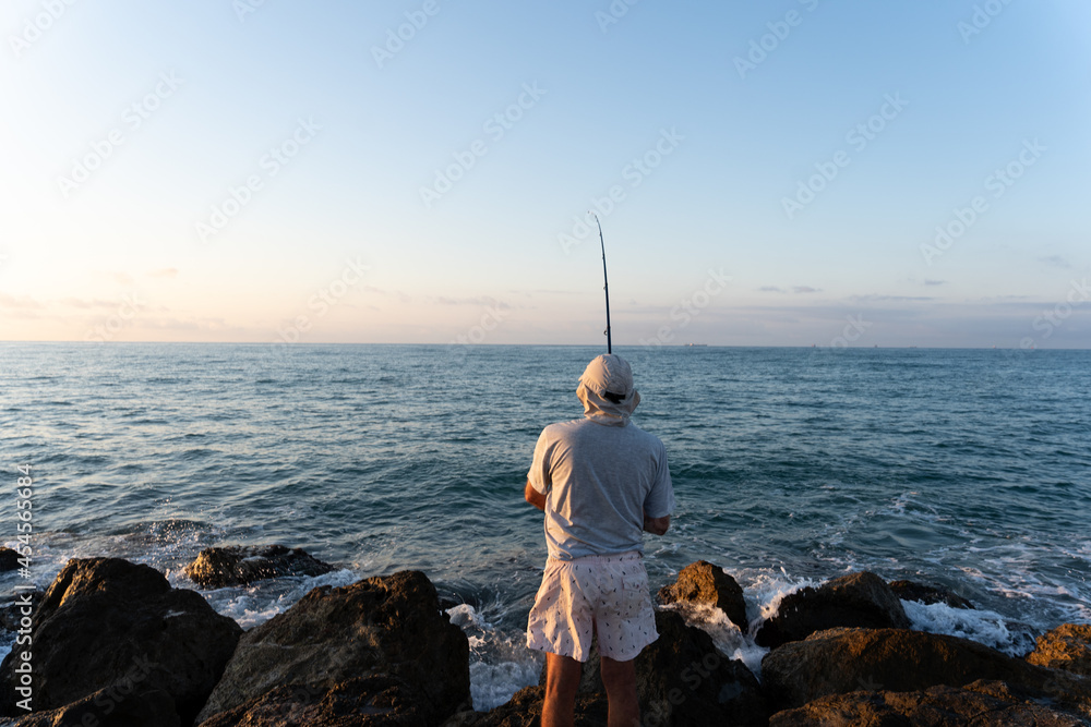Old man fishing by the sea during sunrise