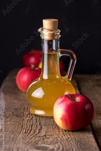 Apple Cider Vinegar in Glass Bottle and Red Fresh Apples Wooden Background Vertical
