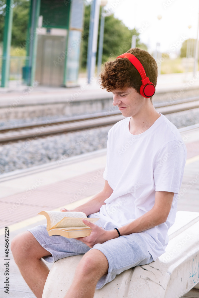 Teen boy reading a red book with red headphones.