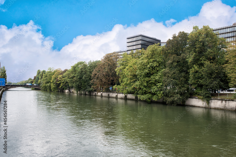 A riverside of Isar river in munich with green trees under blue cloudy sky.