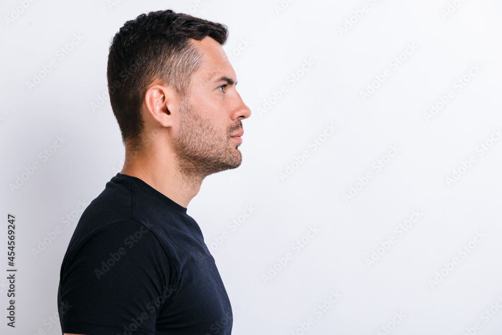 Profile side view portrait of serious calm handsome young bearded man in black shirt standing and looking forward. Indoor studio shot isolated on light white wall background Profile side view portrait of serious calm handsome young bearded man in black shirt standing and looking forward. Indoor studio shot isolated on light white wall background
