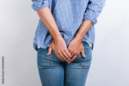 Man suffering from hemorrhoids and anal pain while posing on white background. Male putting his hands at the painful area. Stock photo