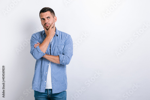 Portrait of pensive handsome bearded young man standing, touching his face, looking aside away and thinking about something. Indoor studio shot, isolated on white background