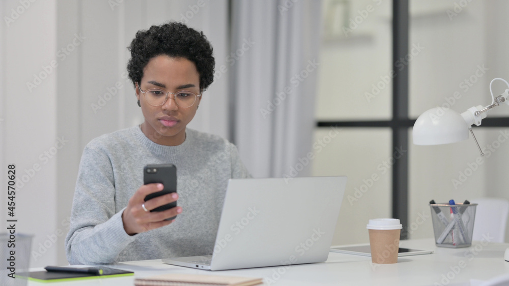 African Woman with Laptop using Smartphone at Work African Woman with Laptop using Smartphone at Work