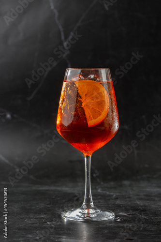 Obraz na płótnie Glass of ice cold Aperol spritz cocktail served in a wine glass, decorated with slices of orange and basil leaf, placed on a black background w salonie