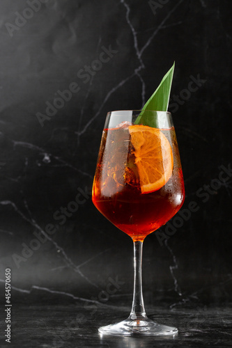Obraz na płótnie Glass of ice cold Aperol spritz cocktail served in a wine glass, decorated with slices of orange and basil leaf, placed on a black background w salonie