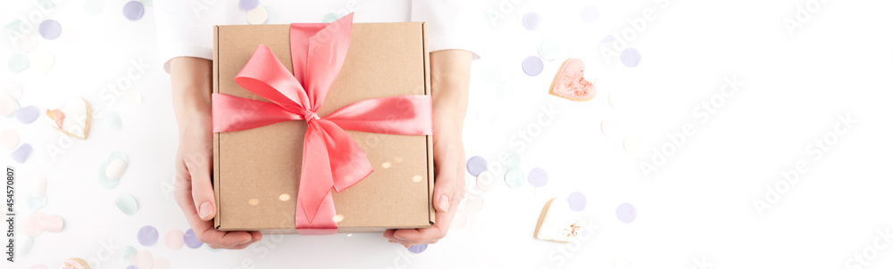woman hands holding gift box with pink bow, confetti, small hearts