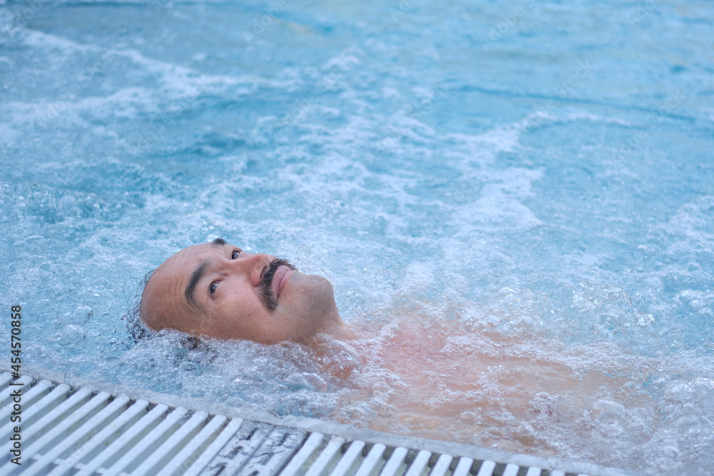 Happy mature asian man laying on water relax in outdoor thermal pool with hydromassage.
