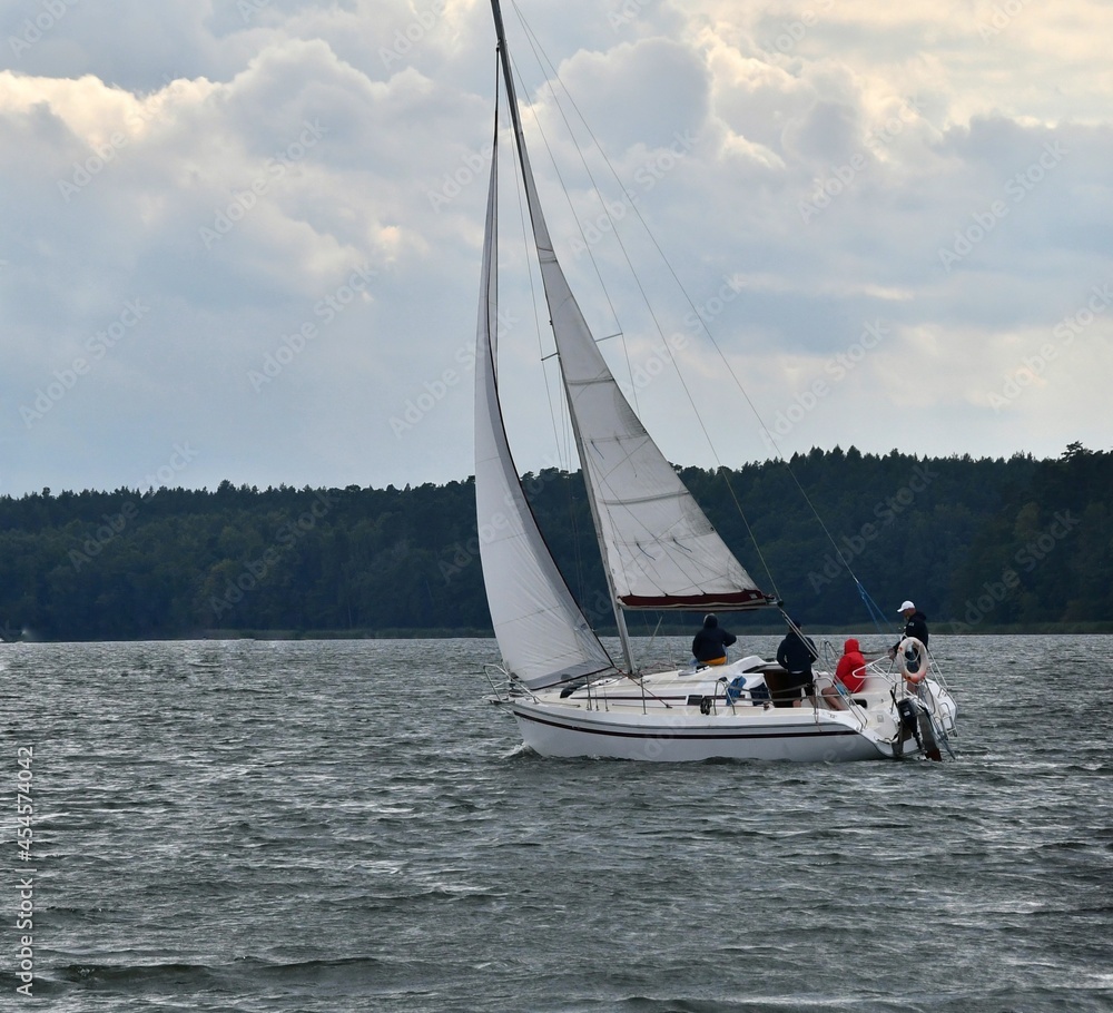 Fototapeta premium Sylwetka samotnie żeglujacego jachtu kabinowego po jeziorze. Mazury, krajobraz.